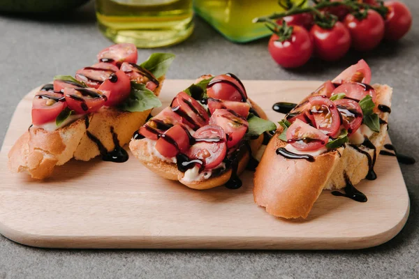 Nahaufnahme köstlicher Bruschetta mit Tomaten und Balsamico auf Holzbrett mit Zutaten — Stockfoto