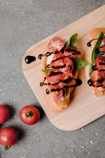 Vista superior de deliciosa bruschetta com balsâmico em tábua de madeira e tomates frescos em cinza — Fotografia de Stock