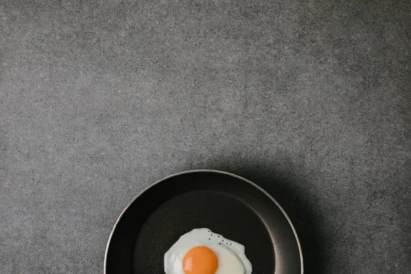 Top view of frying pan with tasty fried egg on grey background — Stock Photo