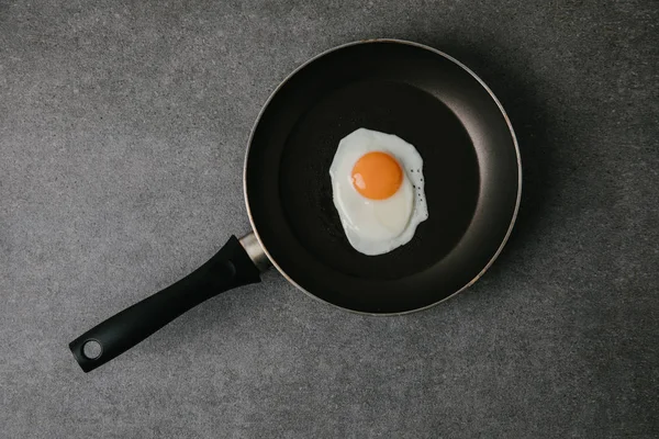 Верхний вид сковородки с вкусным жареным яйцом на сером — стоковое фото
