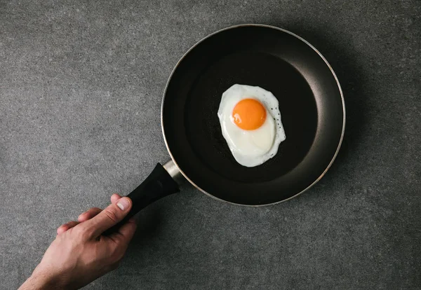 Partial top view of person holding frying pan with fried egg on grey — Stock Photo