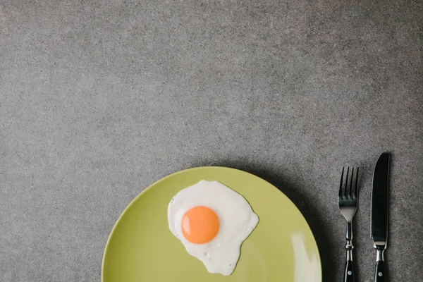 Vista dall'alto uova fresche fritte su piatto e forchetta con coltello su grigio — Foto stock