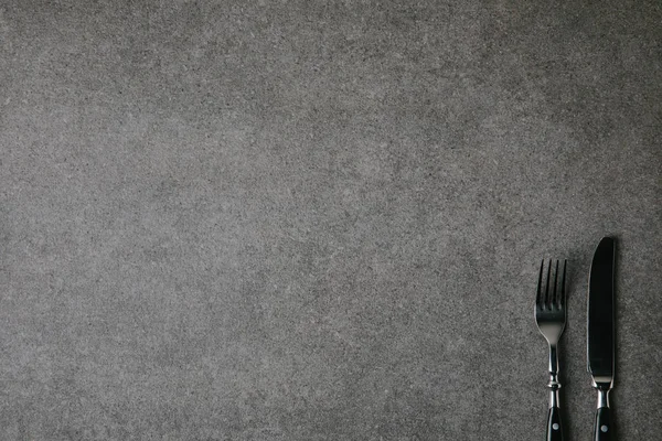 Blick von oben auf glänzende Gabel und Messer auf grauem Hintergrund — Stockfoto