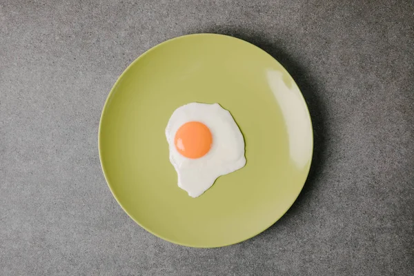 Вид сверху на свежее вкусное жареное яйцо на тарелке на сером — стоковое фото