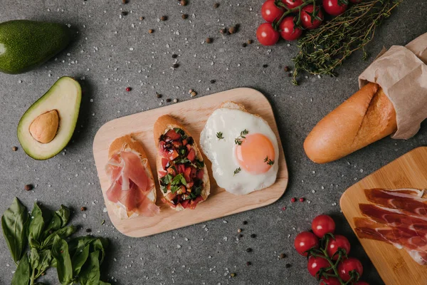 Draufsicht auf Gourmet Antipasto Bruschetta mit Spiegelei und Zutaten auf grau — Stockfoto