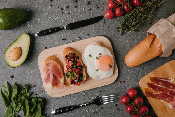 Vista superior de gourmet antipasto bruschetta y huevo frito en tabla de cortar de madera - foto de stock