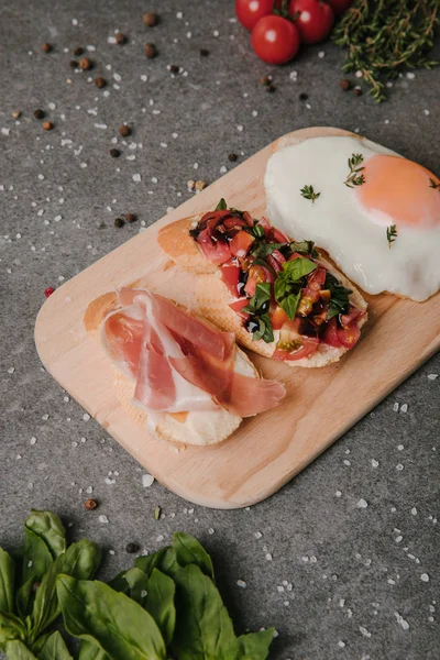 Gourmet antipasto bruschetta and fried egg on wooden cutting board — Stock Photo