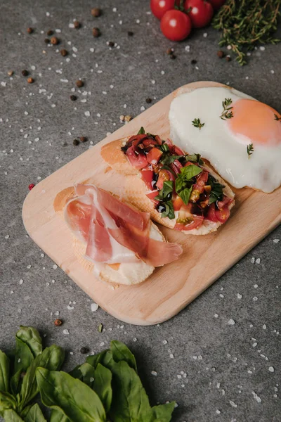 Antipasto bruschetta gourmet y huevo frito en tabla de cortar de madera - foto de stock