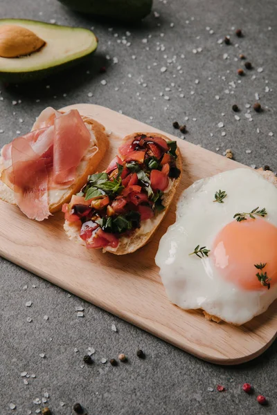 Vista de cerca de la deliciosa bruschetta antipasto y huevo frito en la tabla de cortar de madera - foto de stock