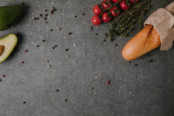 Draufsicht auf frisches Baguette in Papiertüte, Tomaten und Avocado mit Gewürzen auf grau — Stockfoto