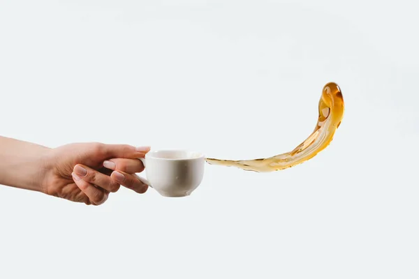 Cropped view of hand holding white cup with splash of aromatic coffee, isolated on white — Stock Photo