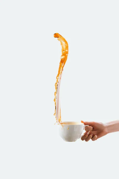 Обрізаний вид руки, що тримає велику білу чашку з бризкою кави, ізольовано на білому — стокове фото