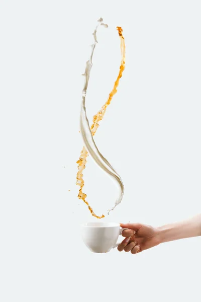 Visão parcial da mão segurando copo branco com salpicos de leite e café aromático, isolado em branco — Fotografia de Stock