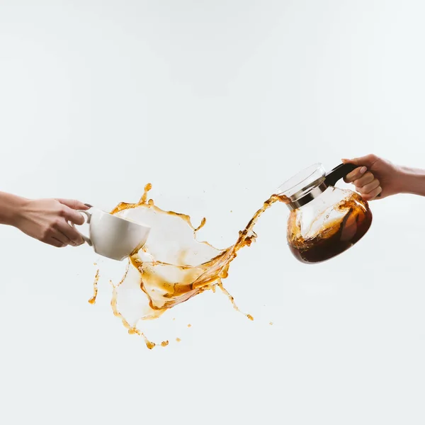 Cropped view of hands with cup and glass pot with splashes of coffee, isolated on white — Stock Photo