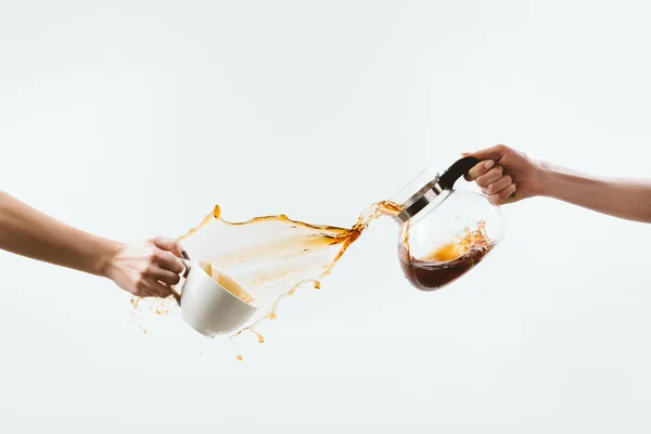 Cropped view of hands with cup and glass pot making splash of coffee, isolated on white — Stock Photo