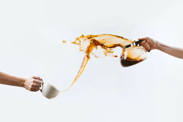 Vista recortada de las manos salpicando café aromático de taza y maceta de vidrio, aislado en blanco - foto de stock
