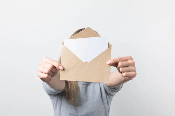 Vista parcial de la mujer que muestra el sobre kraft con tarjeta en blanco en las manos aisladas en blanco - foto de stock