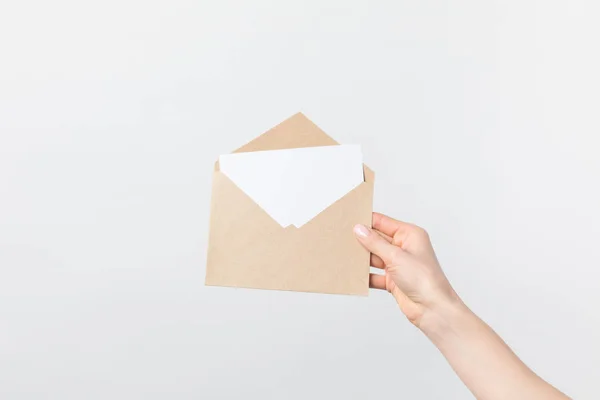 Vue partielle de la femme tenant une enveloppe kraft avec carte blanche à la main isolée sur blanc — Photo de stock