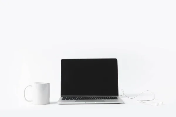 Vue rapprochée de l'ordinateur portable avec écran blanc, écouteurs et tasse blanche isolé sur blanc — Photo de stock