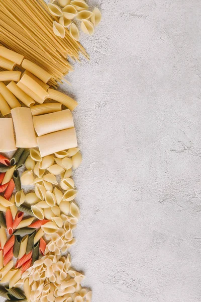 Draufsicht auf verschiedene rohe Pasta auf Betonoberfläche verschüttet — Stockfoto
