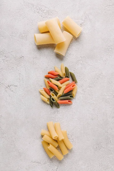 Vue de dessus des piles de différentes pâtes crues en rangée sur la surface du béton — Photo de stock