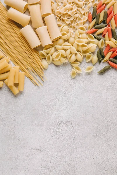 Draufsicht auf verschiedene rohe Pasta auf Betonoberfläche verschüttet — Stockfoto