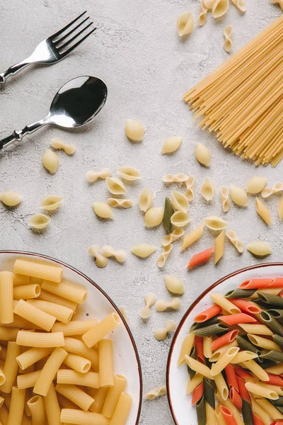 Top view of various raw pasta and cutlery on messy concrete tabletop — Stock Photo