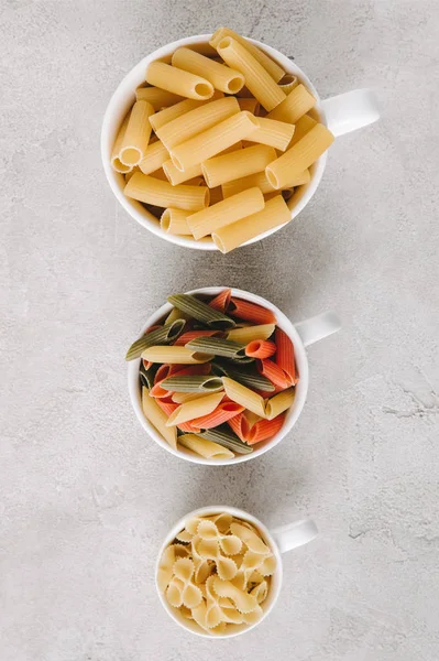 Top view of various types of raw pasta in bowls standing in row on concrete tabletop — Stock Photo