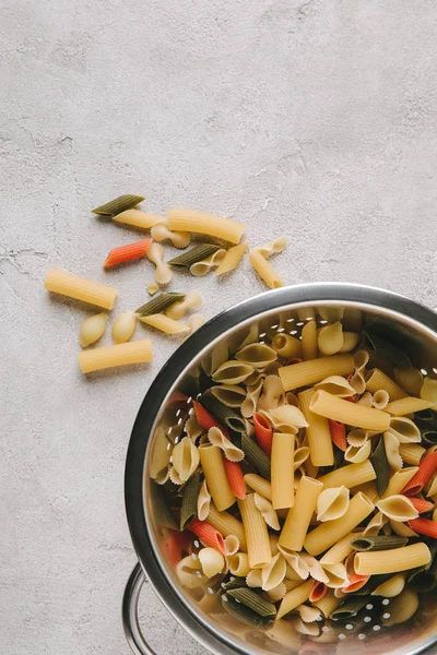 Top view of various types of raw pasta in colander on concrete tabletop — Stock Photo