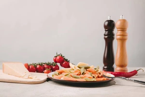 Pasta colorata su piatto con pomodori, formaggio e spezie su superficie di cemento — Foto stock