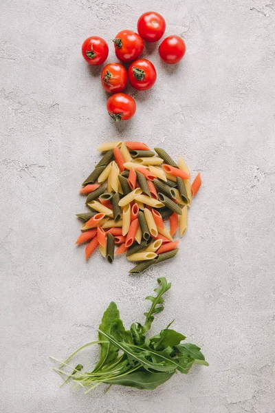 Vista dall'alto di pasta cruda colorata con pomodori e rucola sulla superficie di cemento — Foto stock