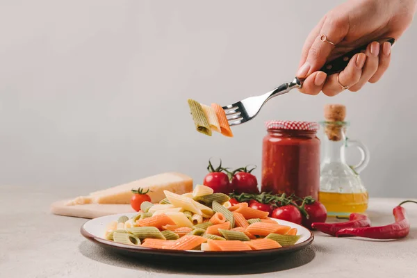 Colpo ritagliato di donna mangiare pasta colorata con forchetta su tavolo di cemento — Foto stock