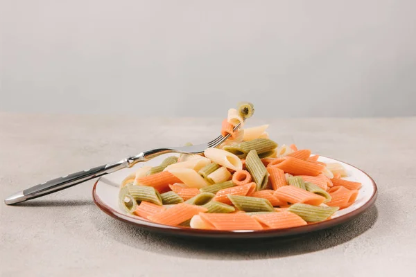 Pâtes colorées sur plaque avec fourchette sur surface en béton — Photo de stock