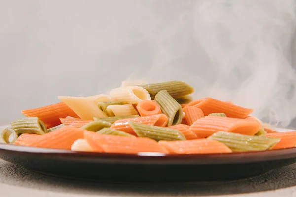 Close-up shot of colorful penne pasta steaming on plate on concrete tabletop — Stock Photo