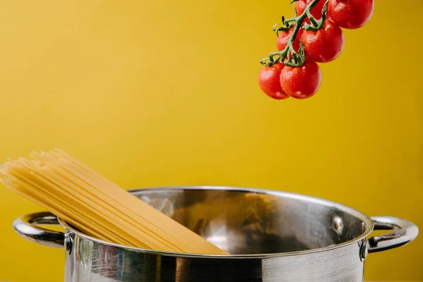 Spaghetti boiling in stewpot with branch of cherry tomatoes above isolated on yellow — Stock Photo