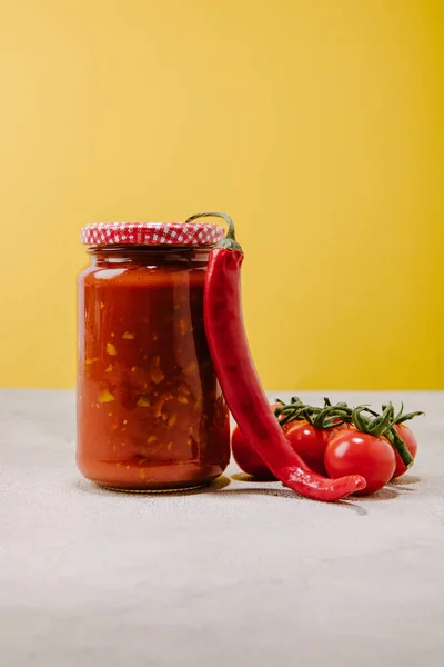 Canned ketchup with chilli pepper and cherry tomatoes on concrete surface — Stock Photo