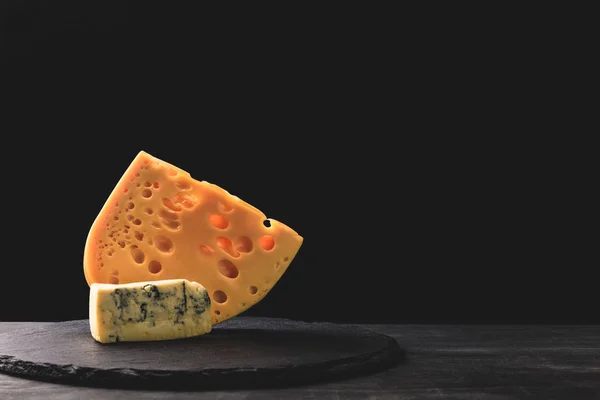 Close up view of emmental and blue cheese on board on black — Stock Photo