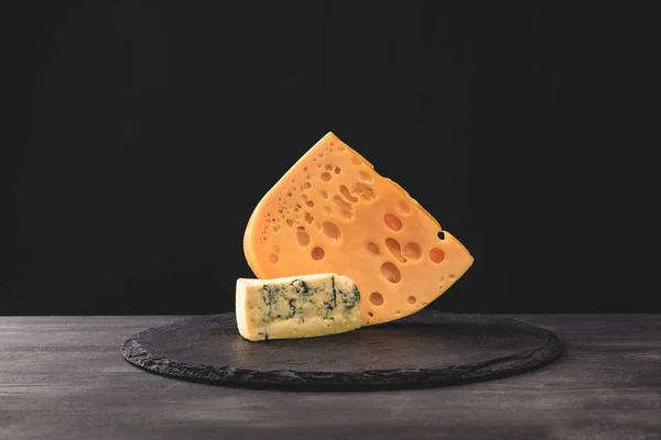 Closeup view of emmental and blue cheese on board on black — Stock Photo