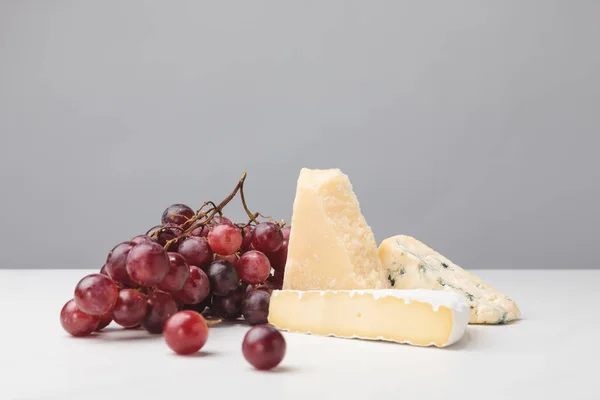 Close up view of brie, cheddar and blue cheese with grapes on gray — Stock Photo