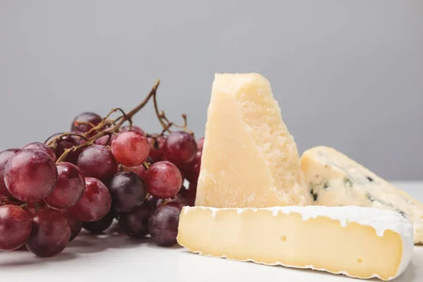 Vue rapprochée de trois types de fromages et de raisins sur gris — Photo de stock