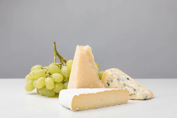 Vue rapprochée de trois types de fromages et de raisins sur gris — Photo de stock