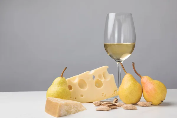 Fromage cheddar et maasdam, poires, amandes et verre à vin sur gris — Photo de stock