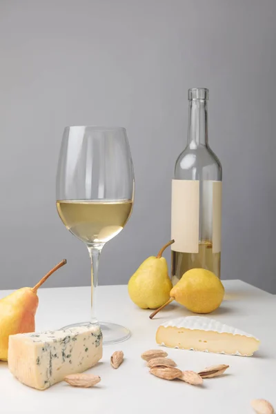 Brie y queso dorblu con peras, almendras, copa de vino y botella en gris - foto de stock