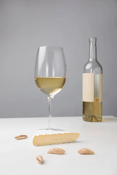 Vista de cerca de queso brie, almendra, copa de vino y botella en gris - foto de stock