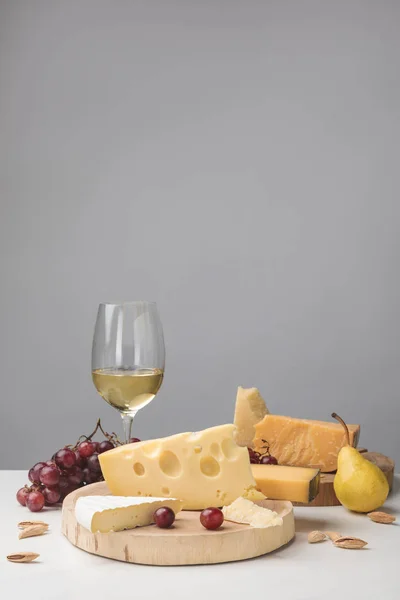 Différents types de fromage sur des planches en bois, verre à vin, fruits et amande sur gris — Photo de stock