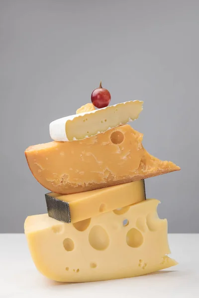 Grape on top of stack of different types of cheese on gray — Stock Photo