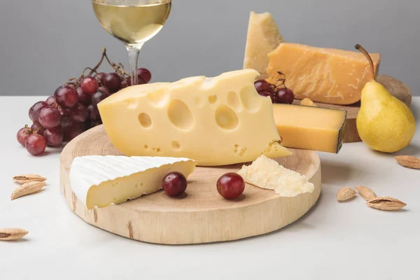 Diversi tipi di formaggio su tavole di legno, bicchiere di vino, frutta e mandorla su grigio — Foto stock