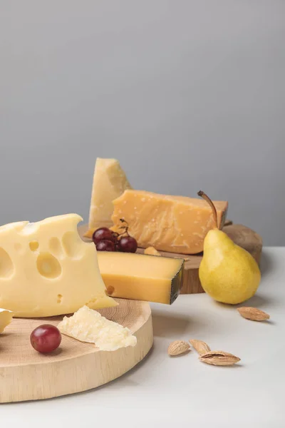 Closeup shot of different types of cheese on wooden boards with grapes and pear on gray — Stock Photo