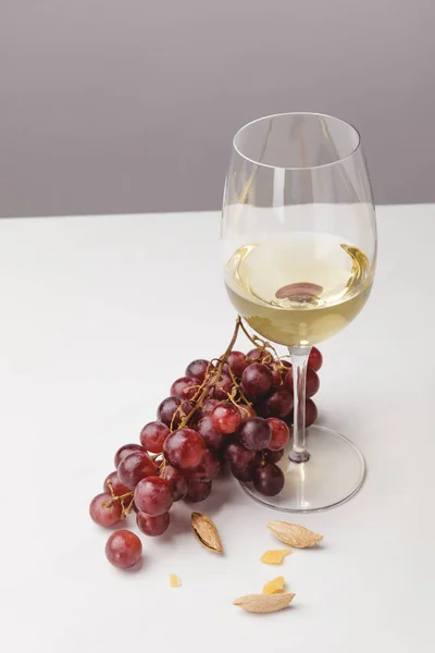 Closeup view of white wine glass, grapes and almond on gray — Stock Photo