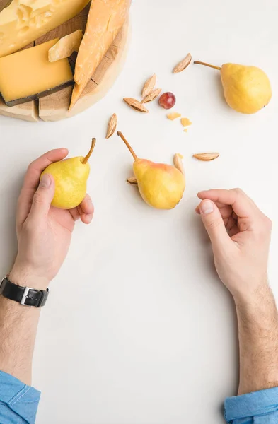 Cropped image of man with pear, almond and different types of cheese on wooden board on white — Stock Photo